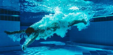 Adam havuz içine atlıyor. Adam yüzme havuzunda su altında yüzüyor.