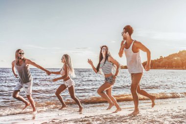 Grup genç çekici arkadaşlar plajda, çalışan ve günbatımı üzerinde gülümseyen eğlenceli olması.
