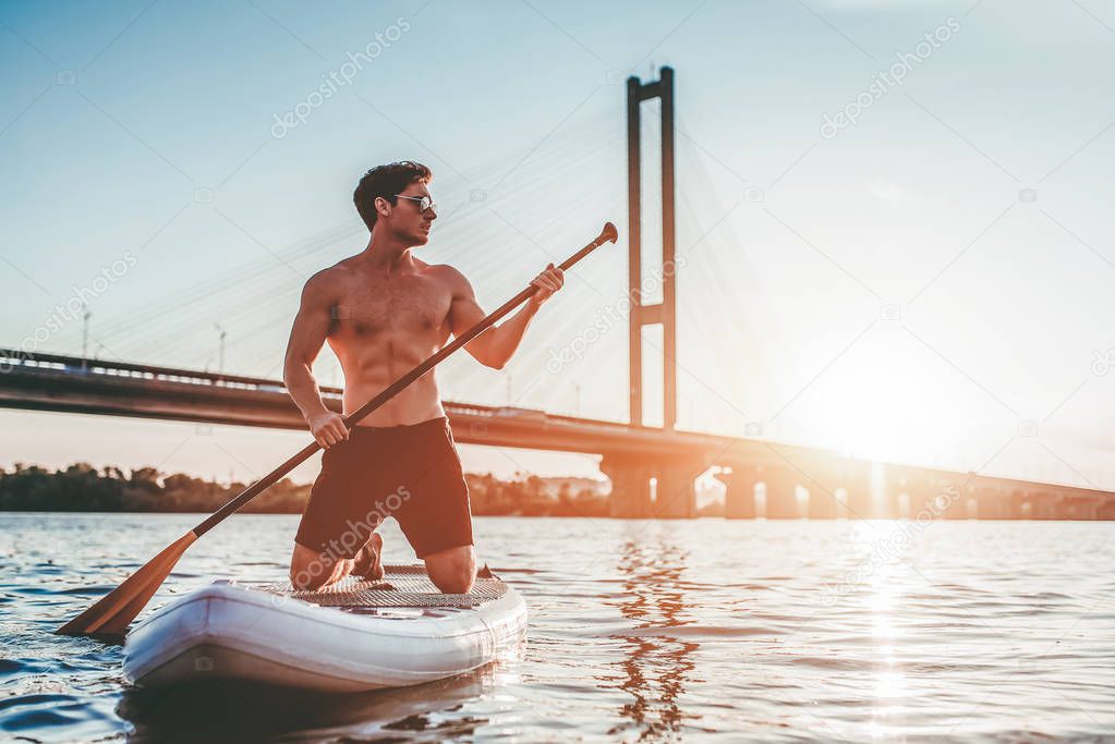 Man on stand up paddle board. Having fun on SUP board during sunset. Active lifestyle.