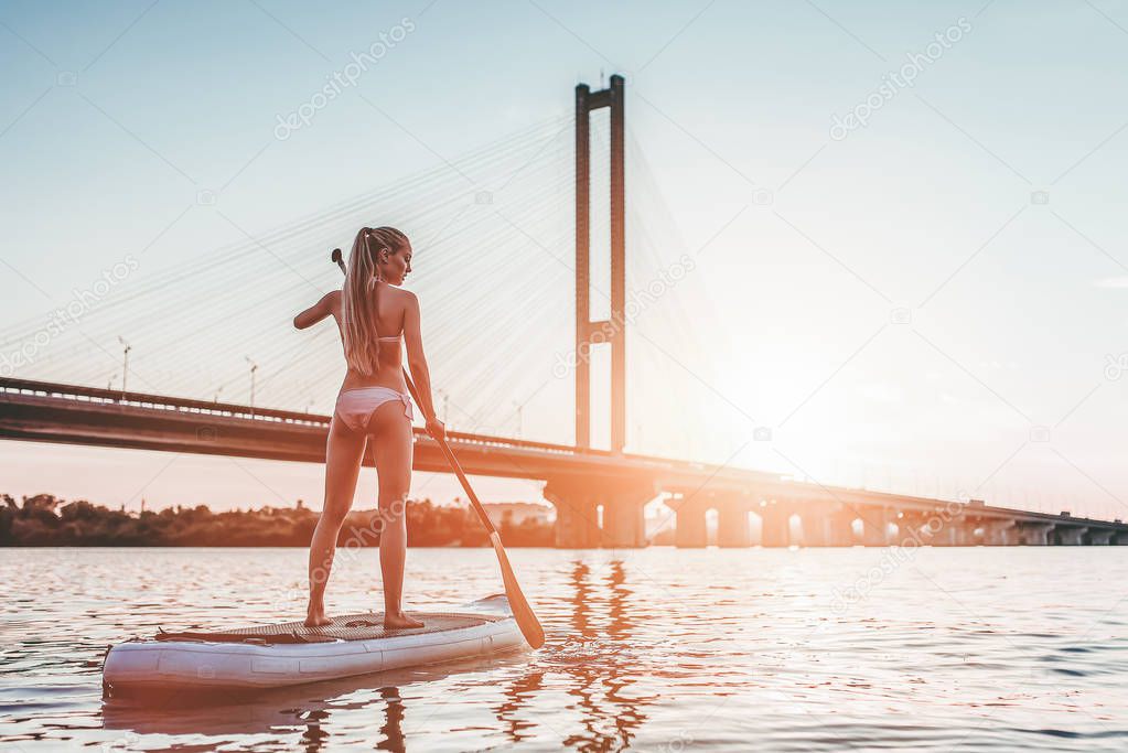 Woman on stand up paddle board. Having fun on SUP board during sunset. Active lifestyle.
