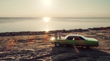 Romantik çift sahilde yeşil retro car yakınındaki duruyor. Sakallı yakışıklı ve çekici genç kadın eski model klasik araba. Aşk hikayesi.