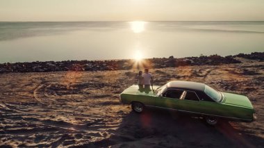 Romantik çift sahilde yeşil retro car yakınındaki duruyor. Sakallı yakışıklı ve çekici genç kadın eski model klasik araba. Aşk hikayesi.