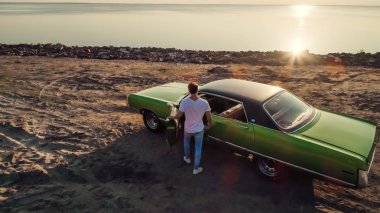 Yakışıklı sakallı adam onun yeşil retro araba ayakta sahilde yürüyor. Vintage Klasik Otomobil.