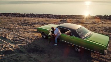 Yakışıklı sakallı adam onun yeşil retro araba ayakta sahilde yürüyor. Vintage Klasik Otomobil.