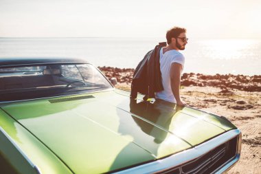 Sakallı yakışıklı yeşil retro arabasını sahilde yakın duruyor. Vintage Klasik Otomobil.