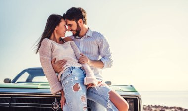 Romantik çift sahilde yeşil retro car yakınındaki duruyor. Sakallı yakışıklı ve çekici genç kadın eski model klasik araba. Aşk hikayesi.