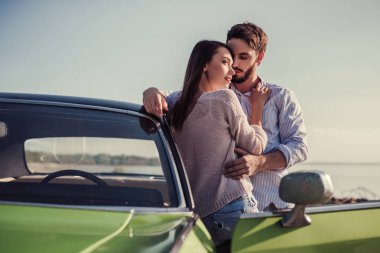 Romantik çift sahilde yeşil retro car yakınındaki duruyor. Sakallı yakışıklı ve çekici genç kadın eski model klasik araba. Aşk hikayesi.