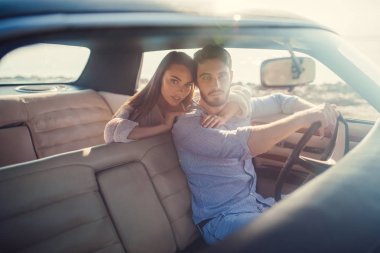 Romantik çift sahilde yeşil retro arabada oturuyor. Sakallı yakışıklı ve çekici genç kadın vintage klasik araba. Şık aşk hikayesi. Sarılma ve öpüşme arabaya olurken.