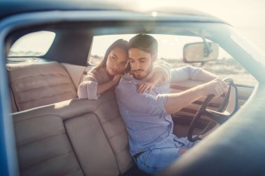 Romantik çift sahilde yeşil retro arabada oturuyor. Sakallı yakışıklı ve çekici genç kadın vintage klasik araba. Şık aşk hikayesi. Sarılma ve öpüşme arabaya olurken.