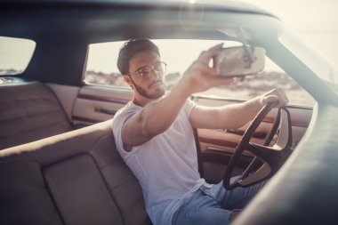 Yakışıklı sakallı adam onun yeşil retro araba ayakta sahilde oturuyor. Vintage Klasik Otomobil.