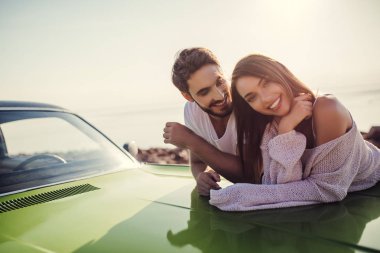 Romantik çift sahilde yeşil retro car yakınındaki duruyor. Sakallı yakışıklı ve çekici genç kadın eski model klasik araba. Aşk hikayesi.