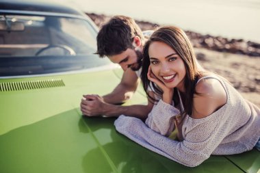 Romantik çift sahilde yeşil retro car yakınındaki duruyor. Sakallı yakışıklı ve çekici genç kadın eski model klasik araba. Aşk hikayesi.