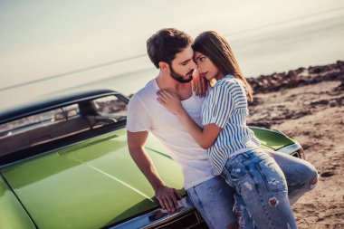 Romantik çift sahilde yeşil retro car yakınındaki duruyor. Sakallı yakışıklı ve çekici genç kadın eski model klasik araba. Aşk hikayesi.