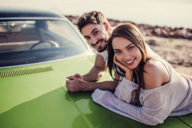 Romantik çift sahilde yeşil retro car yakınındaki duruyor. Sakallı yakışıklı ve çekici genç kadın eski model klasik araba. Aşk hikayesi.