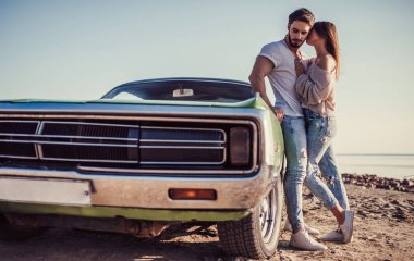 Romantik çift sahilde yeşil retro car yakınındaki duruyor. Sakallı yakışıklı ve çekici genç kadın eski model klasik araba. Aşk hikayesi.