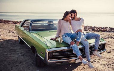 Romantik Çift yeşil retro araba sahilde oturuyor. Sakallı yakışıklı ve çekici genç kadın eski model klasik araba. Aşk hikayesi.