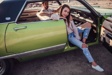 Romantik çift sahilde yeşil retro arabada oturuyor. Sakallı yakışıklı ve çekici genç kadın vintage klasik araba. Şık aşk hikayesi.
