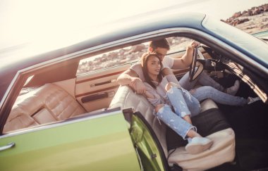 Romantik çift sahilde yeşil retro arabada oturuyor. Sakallı yakışıklı ve çekici genç kadın vintage klasik araba. Şık aşk hikayesi. Sarılma ve öpüşme arabaya olurken.