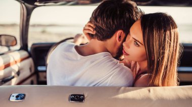 Romantik çift sahilde yeşil retro arabada oturuyor. Sakallı yakışıklı ve çekici genç kadın vintage klasik araba. Şık aşk hikayesi. Sarılma ve öpüşme arabaya olurken.