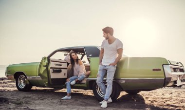 Romantik çift sahilde yeşil retro car yakınındaki duruyor. Sakallı yakışıklı ve çekici genç kadın eski model klasik araba. Aşk hikayesi.