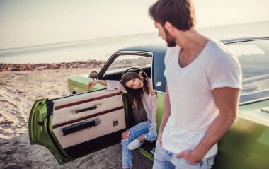 Romantik çift sahilde yeşil retro car yakınındaki duruyor. Sakallı yakışıklı ve çekici genç kadın eski model klasik araba. Aşk hikayesi.