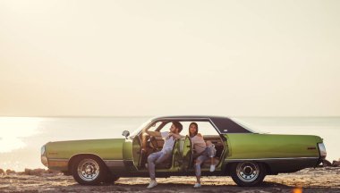 Romantik çift sahilde yeşil retro arabada oturuyor. Sakallı yakışıklı ve çekici genç kadın vintage klasik araba. Şık aşk hikayesi. Sarılma ve öpüşme arabaya olurken.