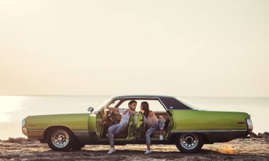 Romantik çift sahilde yeşil retro arabada oturuyor. Sakallı yakışıklı ve çekici genç kadın vintage klasik araba. Şık aşk hikayesi. Sarılma ve öpüşme arabaya olurken.