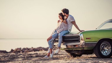 Romantik çift sahilde yeşil retro car yakınındaki duruyor. Sakallı yakışıklı ve çekici genç kadın eski model klasik araba. Aşk hikayesi.