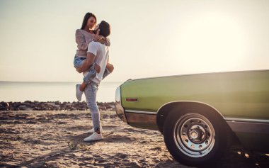 Romantik çift sahilde yeşil retro car yakınındaki duruyor. Sakallı yakışıklı ve çekici genç kadın eski model klasik araba. Aşk hikayesi.