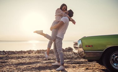 Romantik çift sahilde yeşil retro car yakınındaki duruyor. Sakallı yakışıklı ve çekici genç kadın eski model klasik araba. Aşk hikayesi.