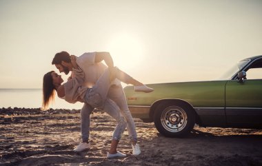 Romantik çift sahilde yeşil retro car yakınındaki duruyor. Sakallı yakışıklı ve çekici genç kadın eski model klasik araba. Aşk hikayesi.