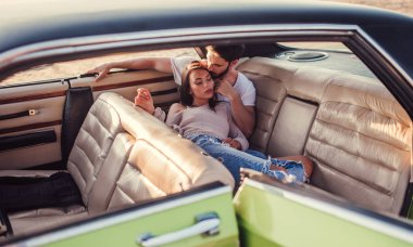 Romantik çift sahilde yeşil retro arabada oturuyor. Sakallı yakışıklı ve çekici genç kadın vintage klasik araba. Şık aşk hikayesi. Sarılma ve öpüşme arabaya olurken.