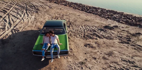 Romantik Çift yeşil retro araba sahilde oturuyor. Sakallı yakışıklı ve çekici genç kadın eski model klasik araba. Aşk hikayesi.