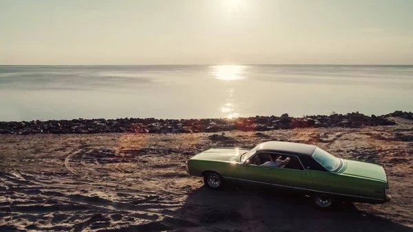 Yakışıklı sakallı adam onun yeşil retro araba ayakta sahilde oturuyor. Vintage Klasik Otomobil.