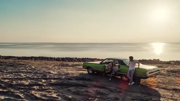 Romantik çift sahilde yeşil retro car yakınındaki duruyor. Sakallı yakışıklı ve çekici genç kadın eski model klasik araba. Aşk hikayesi.
