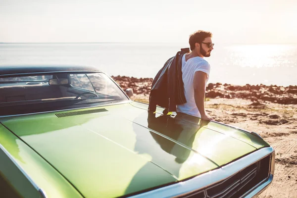 英俊的大胡子男子站在他的绿色复古汽车在海滩上 复古经典车 — 图库照片