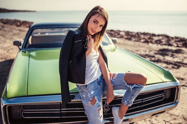 Çekici genç şık kadın yakınındaki plajda yeşil retro araba duruyor. Vintage Klasik Otomobil.