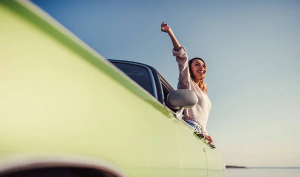 Feel the spirit of adventure! Attractive young woman is leaning out of the window of green retro car. Vintage classic car.