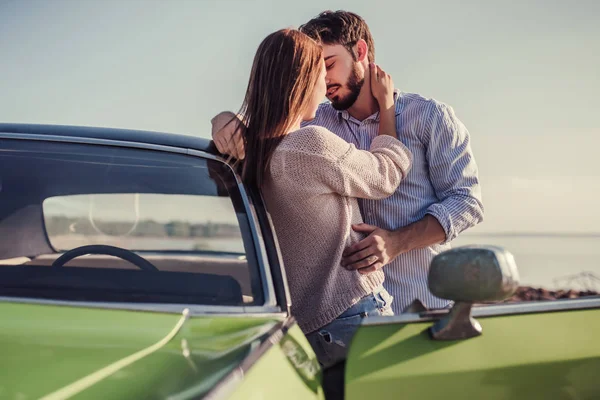 Romantik çift sahilde yeşil retro car yakınındaki duruyor. Sakallı yakışıklı ve çekici genç kadın eski model klasik araba. Aşk hikayesi.