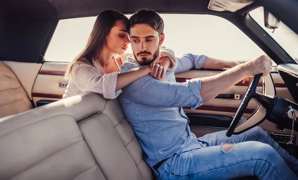 Romantic couple is sitting in green retro car on the beach. Handsome bearded man and attractive young woman in vintage classic car. Stylish love story. Hugging and kissing while being in car.