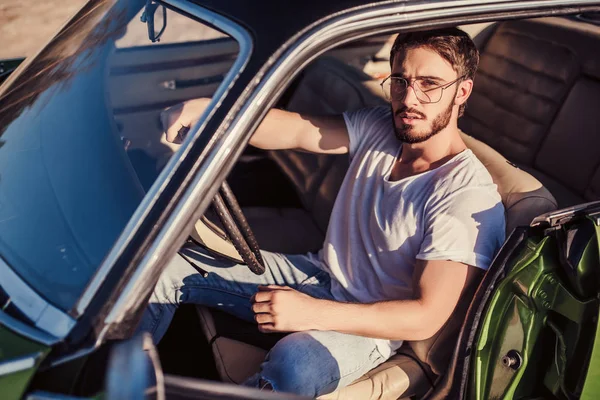 Yakışıklı sakallı adam onun yeşil retro araba ayakta sahilde oturuyor. Vintage Klasik Otomobil.