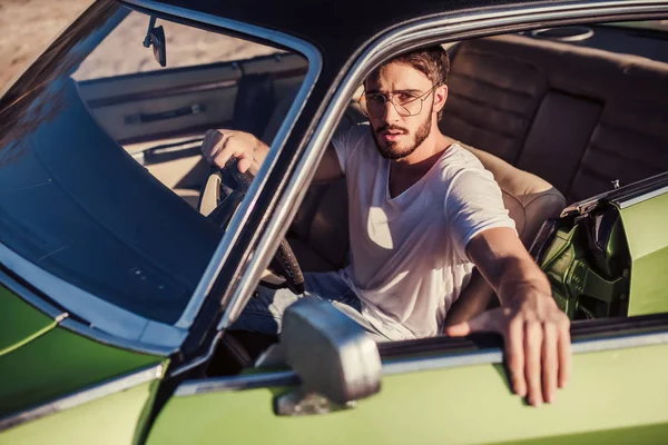 Yakışıklı sakallı adam onun yeşil retro araba ayakta sahilde oturuyor. Vintage Klasik Otomobil.