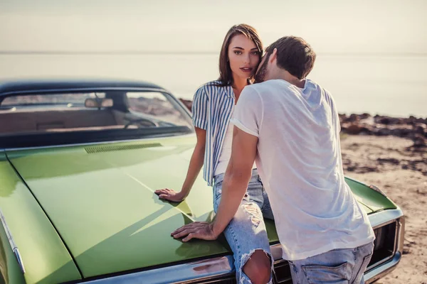 Romantik çift sahilde yeşil retro car yakınındaki duruyor. Sakallı yakışıklı ve çekici genç kadın eski model klasik araba. Aşk hikayesi.