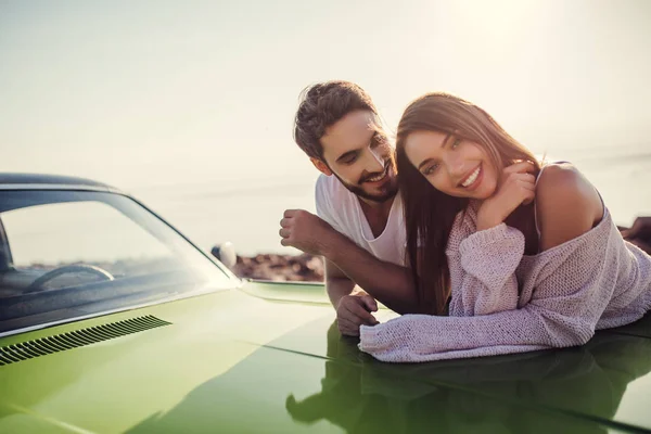 Romantic couple is standing near green retro car on the beach. Handsome bearded man and attractive young woman with vintage classic car. Love story.
