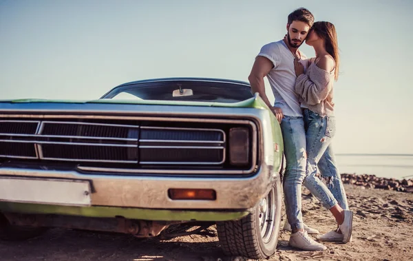 Romantik çift sahilde yeşil retro car yakınındaki duruyor. Sakallı yakışıklı ve çekici genç kadın eski model klasik araba. Aşk hikayesi.