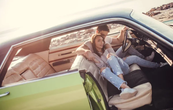 Romantik çift sahilde yeşil retro arabada oturuyor. Sakallı yakışıklı ve çekici genç kadın vintage klasik araba. Şık aşk hikayesi. Sarılma ve öpüşme arabaya olurken.