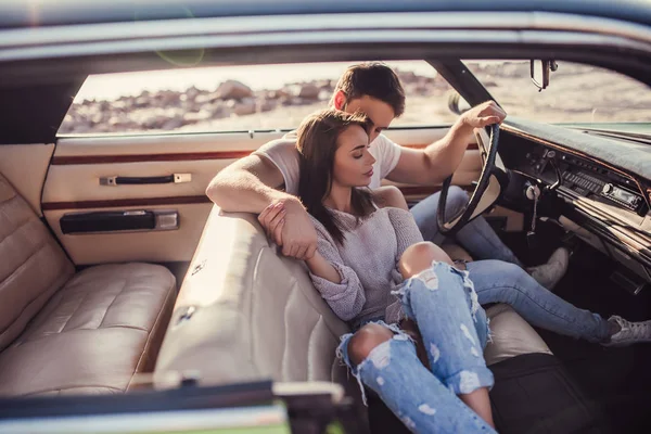 Romantik çift sahilde yeşil retro arabada oturuyor. Sakallı yakışıklı ve çekici genç kadın vintage klasik araba. Şık aşk hikayesi. Sarılma ve öpüşme arabaya olurken.
