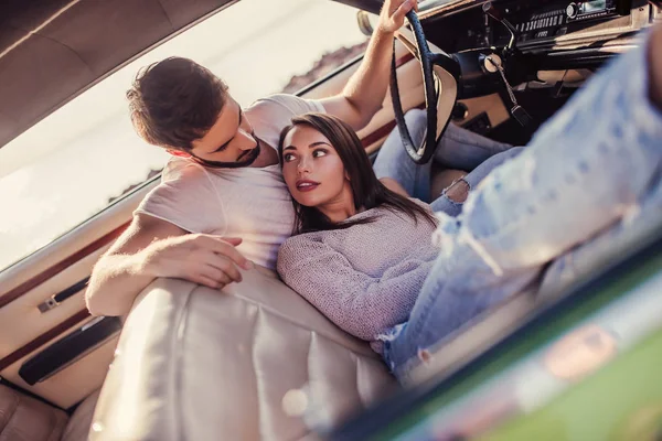 Romantik çift sahilde yeşil retro arabada oturuyor. Sakallı yakışıklı ve çekici genç kadın vintage klasik araba. Şık aşk hikayesi. Sarılma ve öpüşme arabaya olurken.