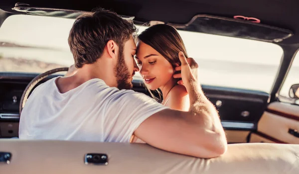 Romantic couple is sitting in green retro car on the beach. Handsome bearded man and attractive young woman in vintage classic car. Stylish love story. Hugging and kissing while being in car.