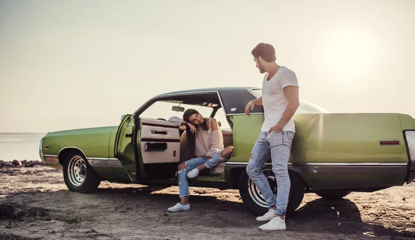 Romantik çift sahilde yeşil retro car yakınındaki duruyor. Sakallı yakışıklı ve çekici genç kadın eski model klasik araba. Aşk hikayesi.